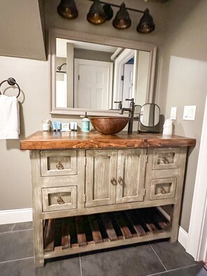 A bathroom vanity with a wooden countertop, a large mirror, a sink, and a wine rack below.