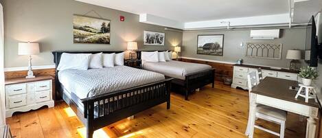 Un dormitorio con dos camas, suelo de madera, mesitas de noche con lámparas, un escritorio con silla y obras de arte en las paredes.