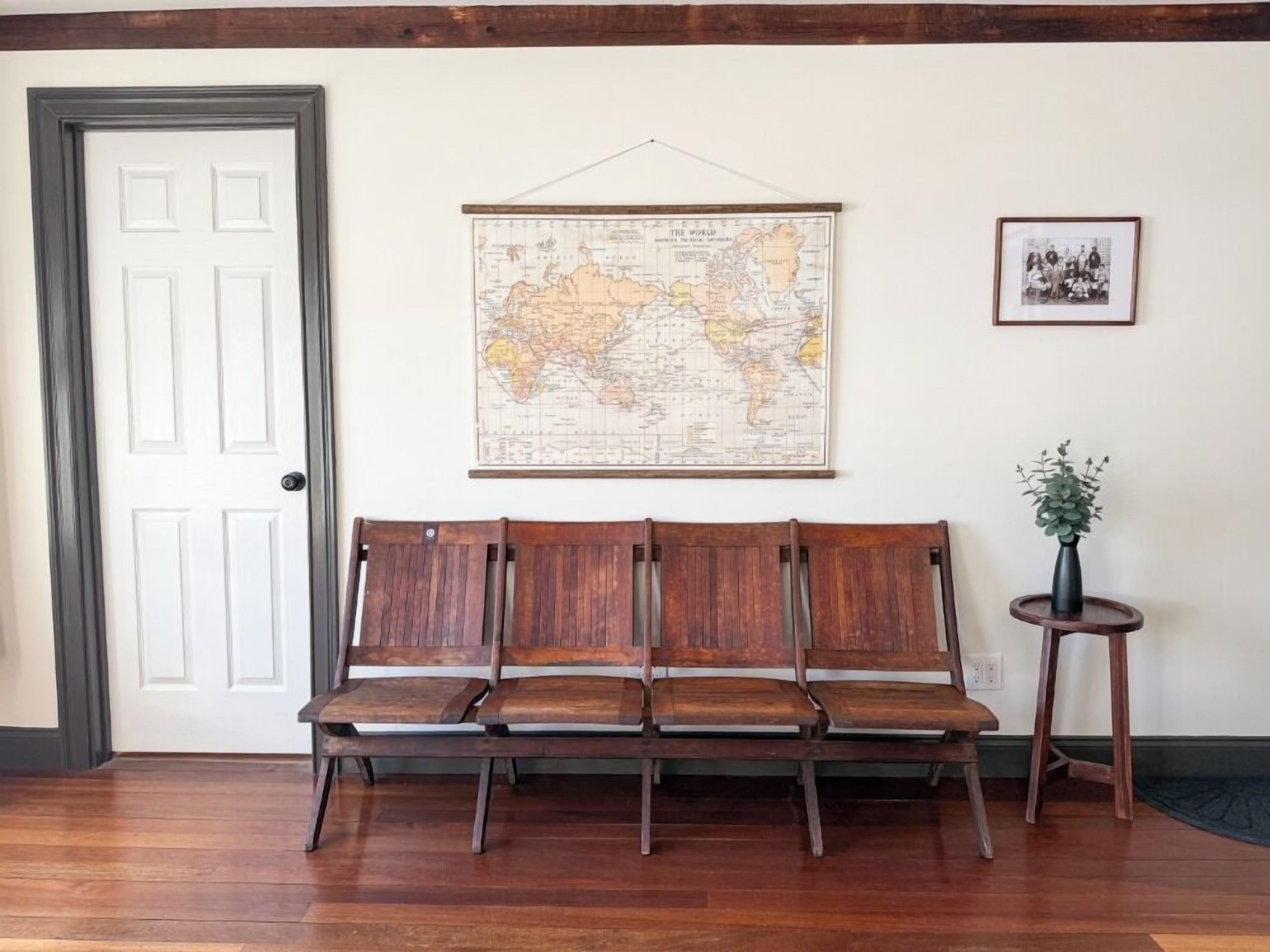 A wooden bench with a map on the wall, a framed photo, and a small table with a plant.