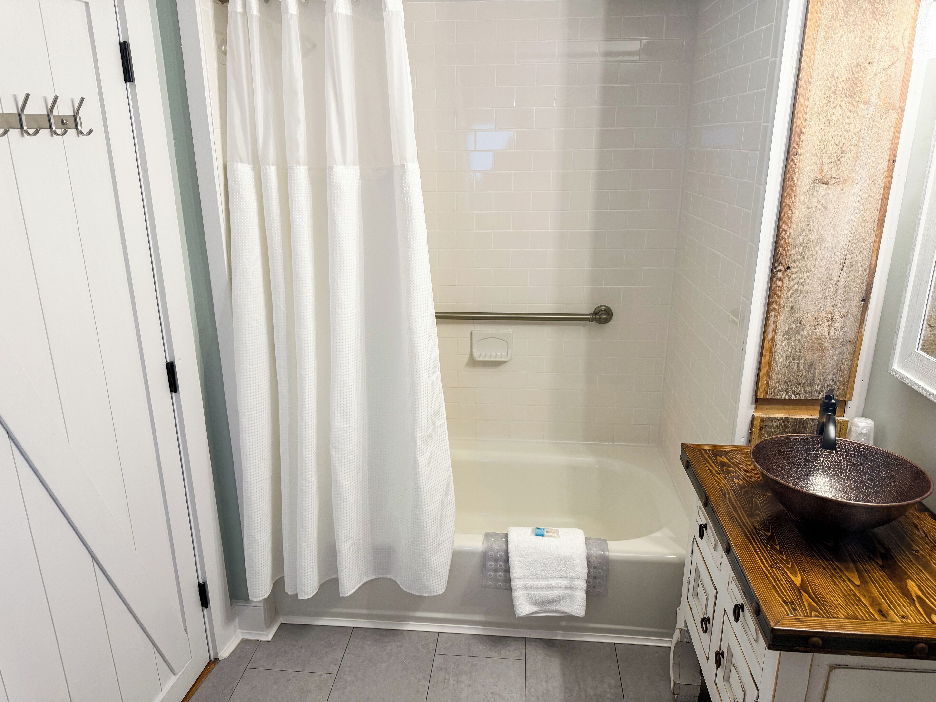 A bathroom with a bathtub, a wooden vanity with a sink, a towel rack, and a shower curtain.