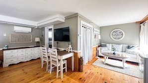 A spacious living area with a wooden floor, a dining table with chairs, a sofa, and a television mounted on the wall. - Black Walnut Inn (Amherst)