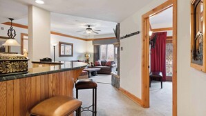 A spacious living area with a wooden bar, a ceiling fan, and a view of the outdoors through a window with red curtains. - The Charter at Beaver Creek D2705 (Beaver Creek)