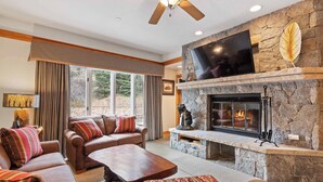 A cozy living room with a stone fireplace, comfortable seating, and a large flat-screen TV mounted above the fireplace. - The Charter at Beaver Creek D2705 (Beaver Creek)
