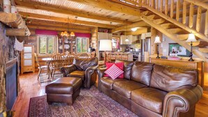 A cozy log cabin interior with a wooden staircase, leather furniture, and a dining area. - 24-0089 Rustic Hartsel Getaway w/ 35-Acre Yard (Fairplay)