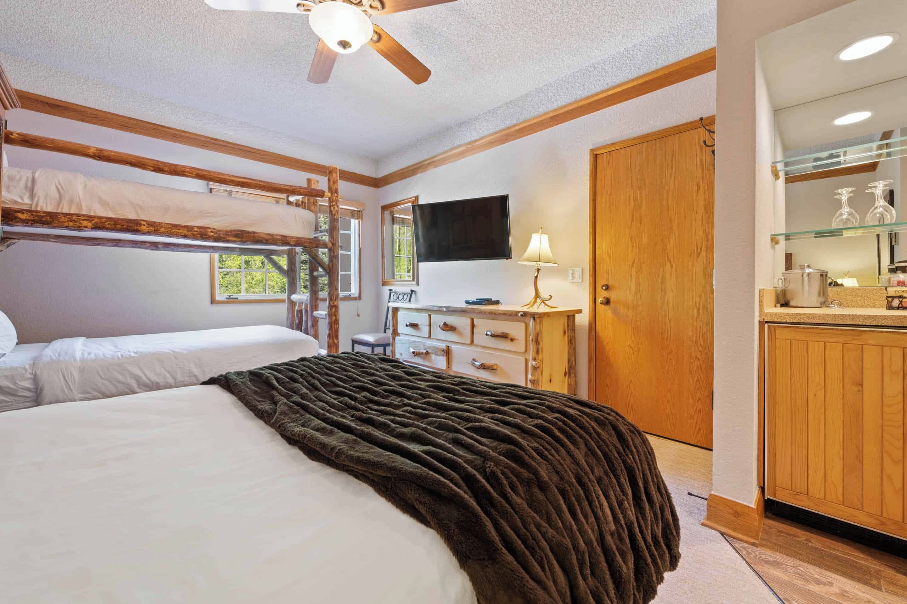 A bedroom with a bunk bed, a desk, a dresser, a television, and a wooden door.