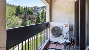 Un balcon équipé d’un climatiseur Mitsubishi Electric, d’une chaise et offrant une vue sur une zone boisée.