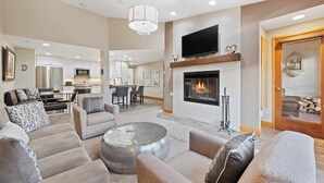 A spacious living room with a fireplace, a television mounted above it, and a dining area in the background. - The Charter at Beaver Creek D4805 (Beaver Creek)