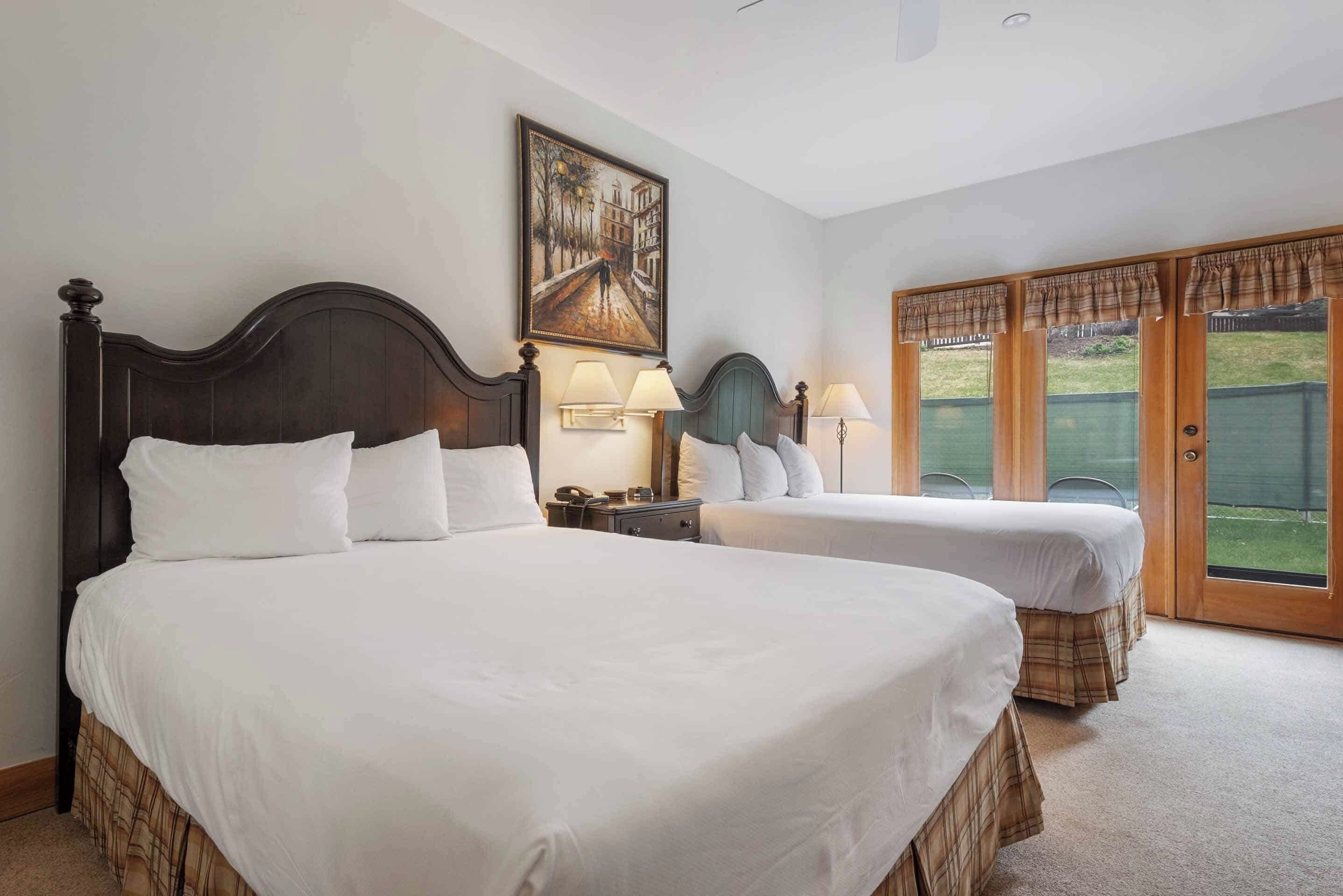 A hotel room with two beds, a painting on the wall, and a view of the outdoors through a sliding door.