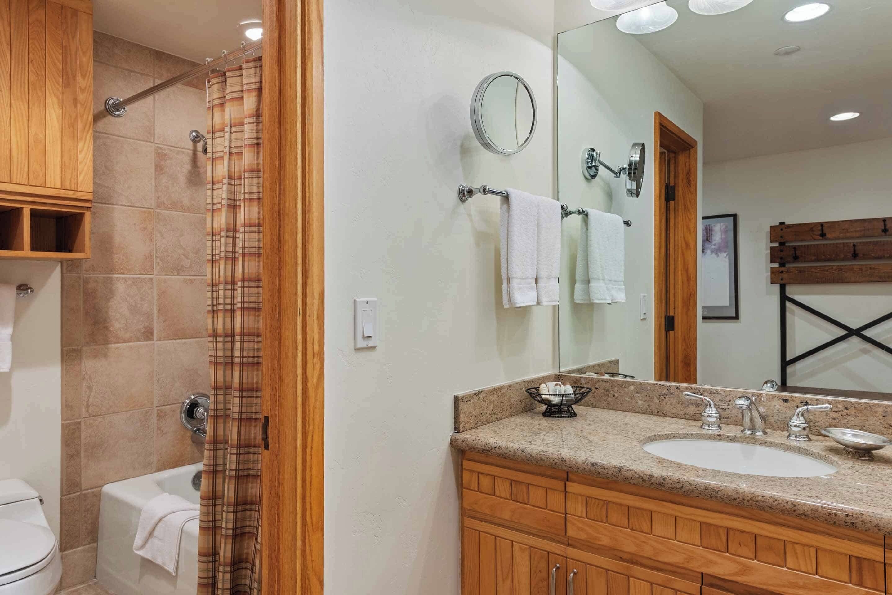 A bathroom with a shower, a toilet, a sink, and wooden cabinets.