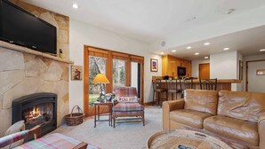 A cozy living room with a fireplace, a television, and a dining area with wooden cabinets and a bar. - The Charter at Beaver Creek E0105 (Beaver Creek)
