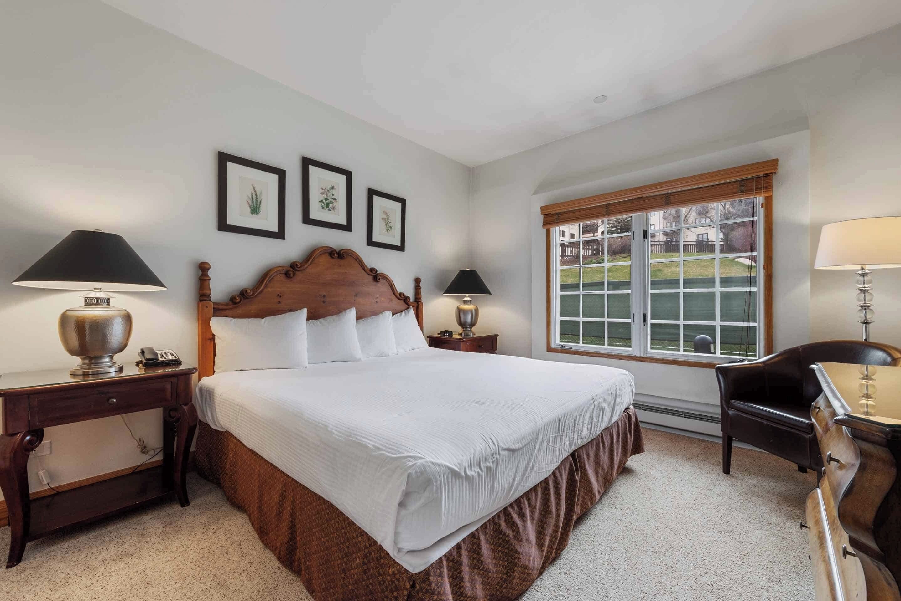 A neatly arranged bedroom with a large bed, two bedside tables with lamps, a wooden headboard, and a window with a view of a backyard.