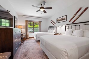 A bedroom with two beds, a ceiling fan, a desk with a lamp, a dresser, and a window with curtains.