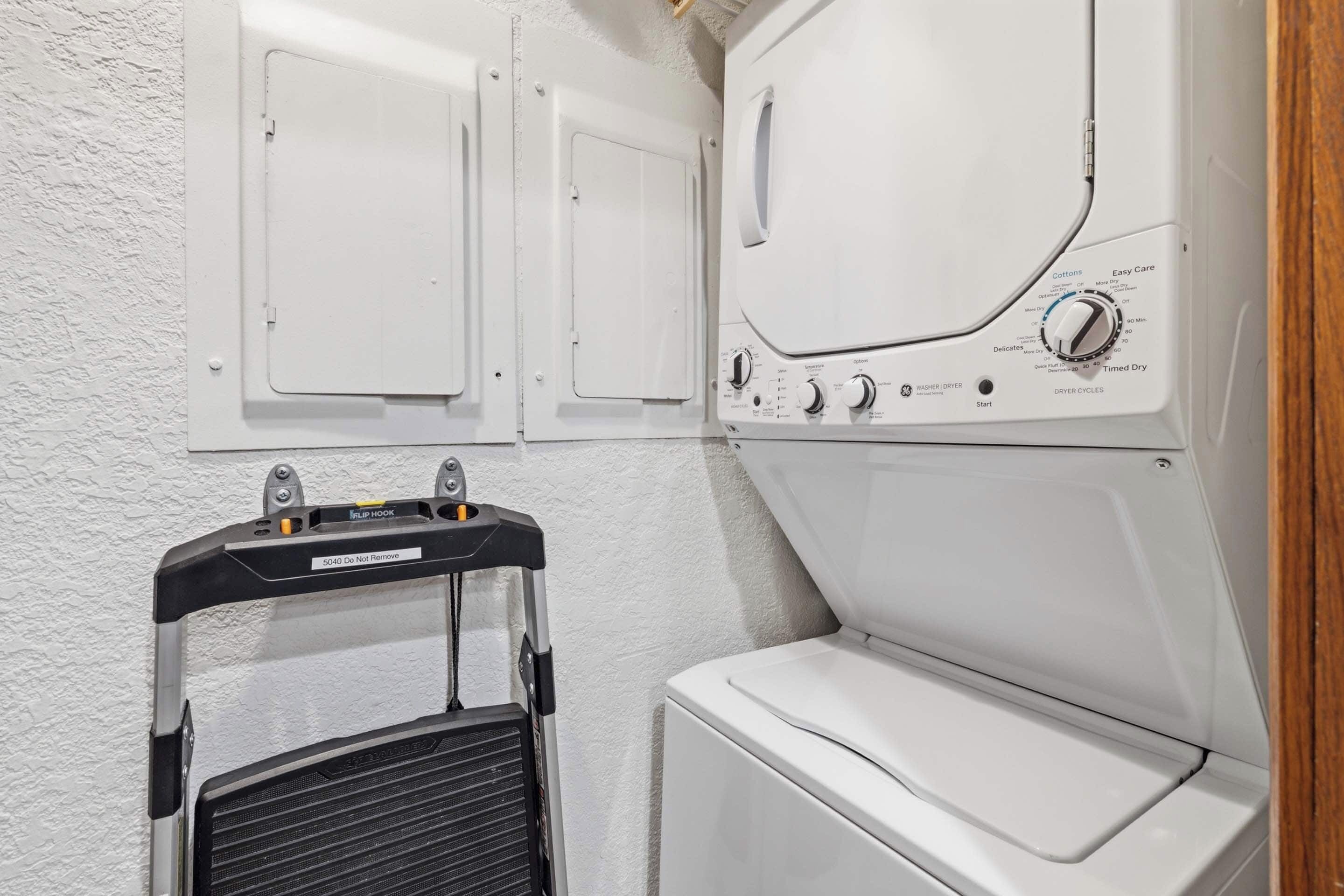 Un espace buanderie comprenant un lave-linge et un sèche-linge à chargement frontal, un étendoir métallique et un meuble fixé au mur.