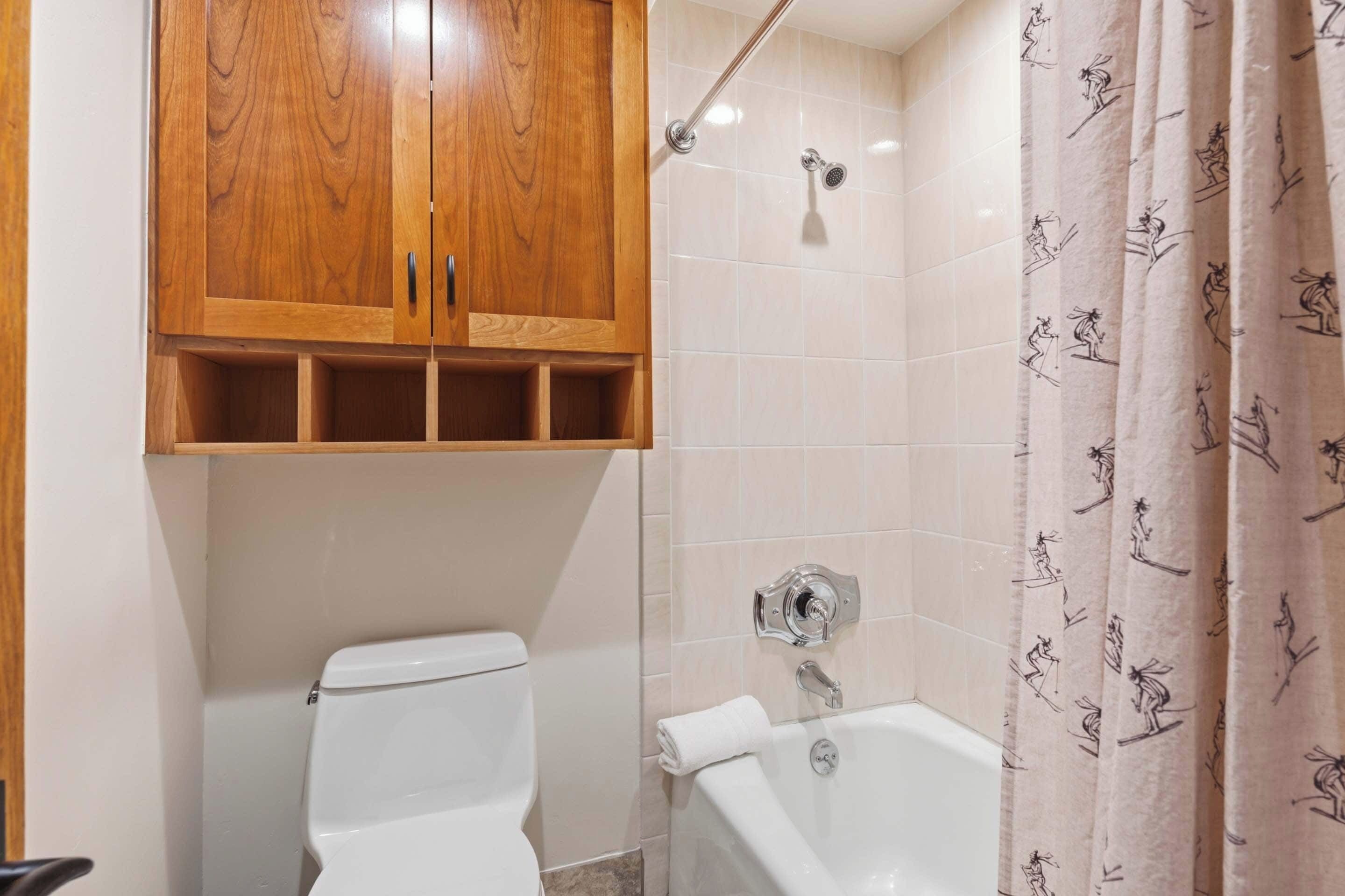 A bathroom with a wooden cabinet, a toilet, a bathtub, and a shower curtain with a pattern.