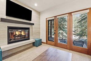A modern living room with a fireplace, a television mounted above it, and a sliding glass door leading to an outdoor area with a view of trees. - The Charter at Beaver Creek E0405 (Beaver Creek)