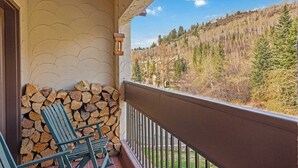 A balcony with stacked firewood, a chair, and a view of a forested hillside. - The Charter at Beaver Creek D4105 (Beaver Creek)
