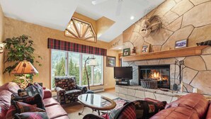 A cozy living room with a fireplace, plaid-patterned furniture, and a large window offering a view of trees. - The Charter at Beaver Creek D4205 (Beaver Creek)