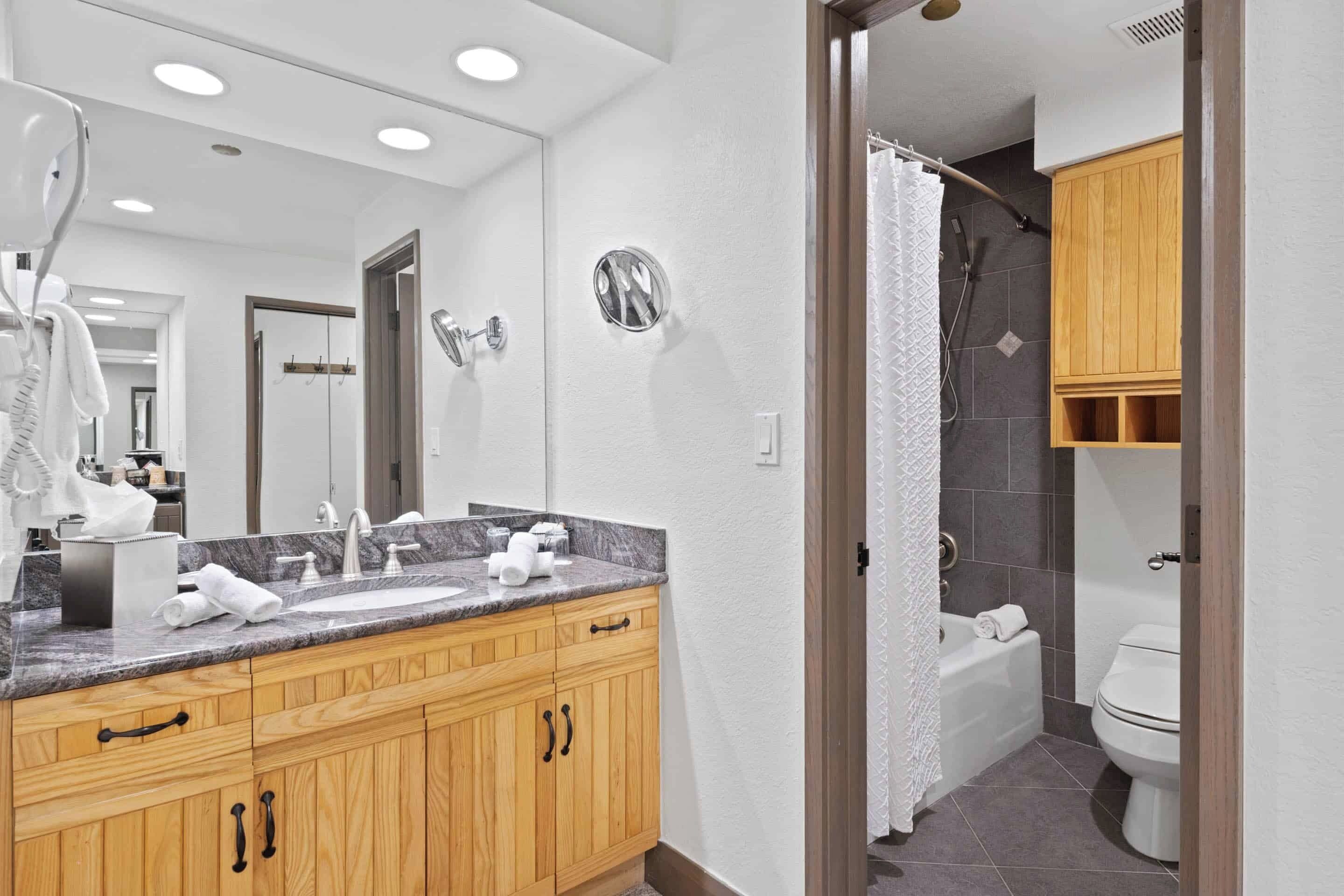 A modern bathroom with wooden cabinets, a marble countertop, a large mirror, and a shower area.