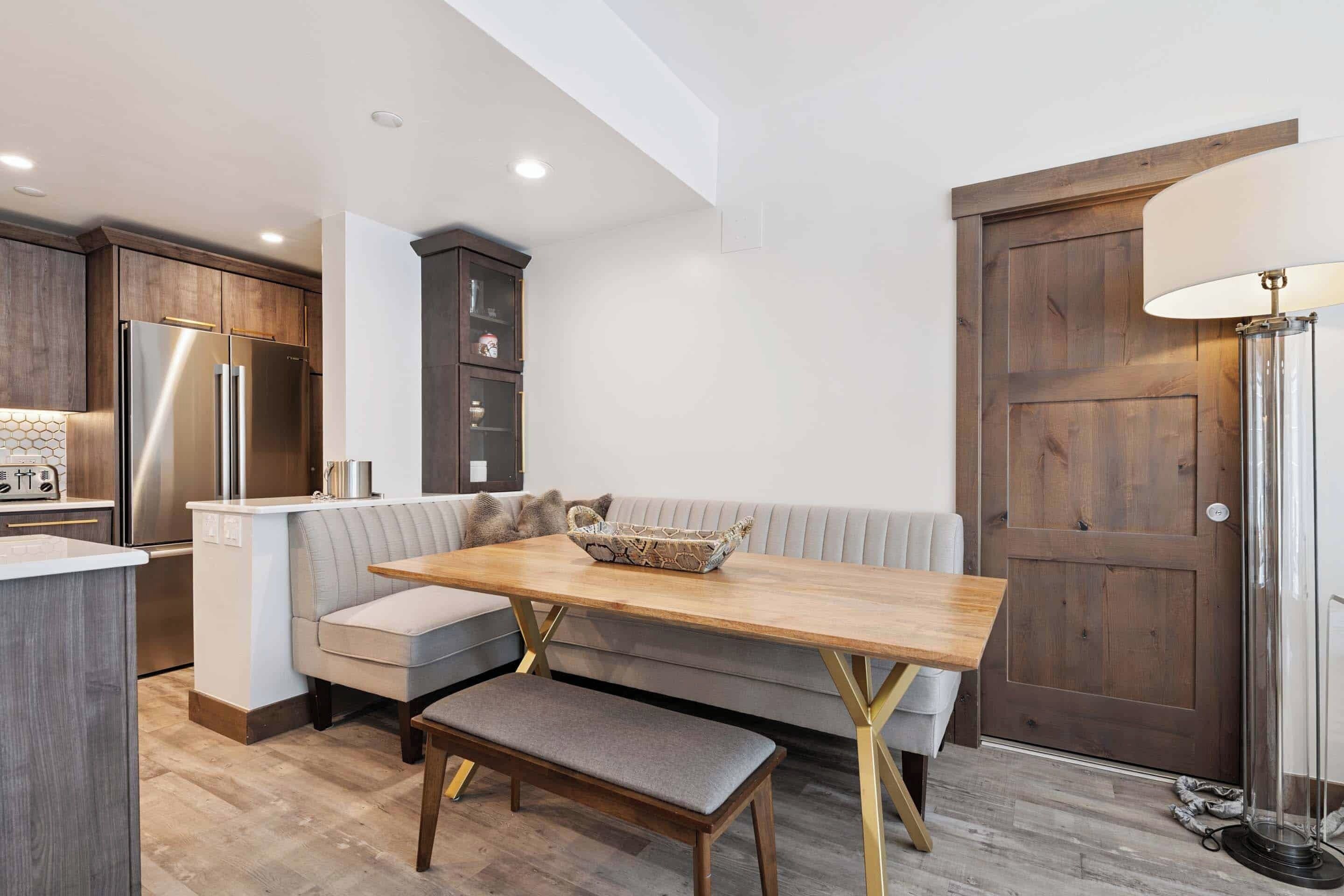 Una cocina compacta con refrigerador empotrado, una mesa de comedor de madera y un banco, y un sofá gris.