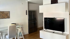 Un saló modern amb bigues de fusta a la vista, televisió de pantalla plana, llar de foc integrada, zona de menjador amb taula i cadires de vidre i un refrigerador.