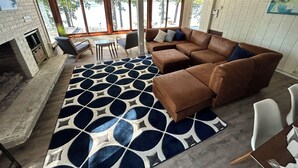 Un salon spacieux, doté d’un canapé d’angle, d’une cheminée et de grandes fenêtres donnant sur l’extérieur.