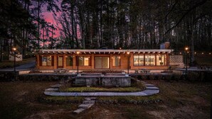 Un chalet doté d’un patio couvert, de meubles d’extérieur et d’un foyer, le tout entouré d’une zone boisée.