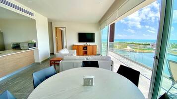 A modern hotel room with a dining area, a flat-screen TV, and a balcony with a view of the ocean.