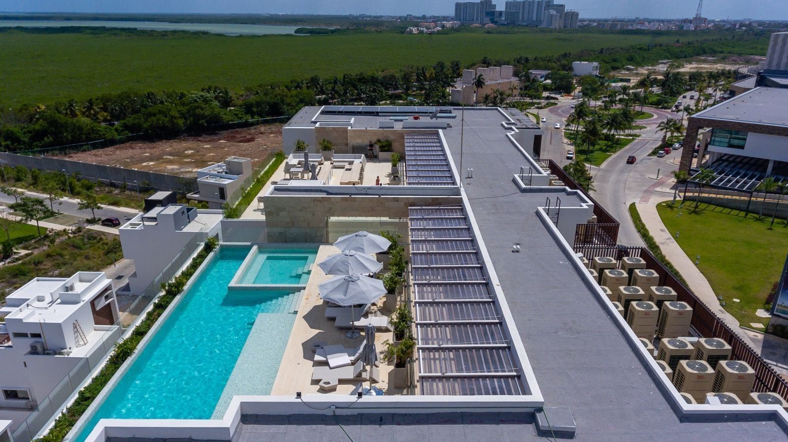 En pool på taket med solstolar och parasoller, omgiven av moderna byggnader och med utsikt över stadens silhuett.