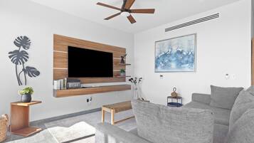 Een moderne woonkamer met een flatscreen-tv, grijze banken, een plafondventilator en een groot abstract schilderij.