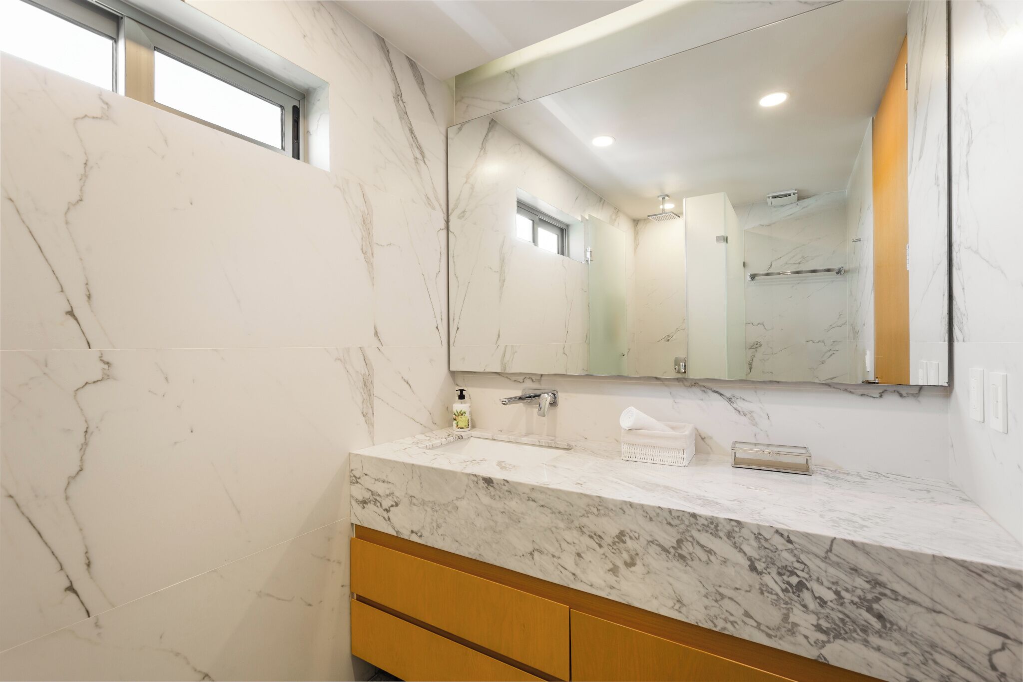Un baño con paredes de mármol, un espejo grande y un tocador de madera.