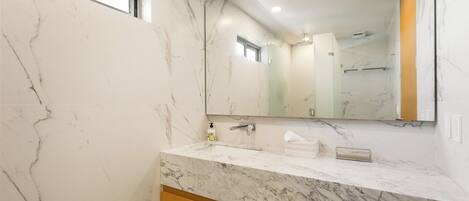 Un baño con paredes de mármol, un espejo grande y un tocador de madera.