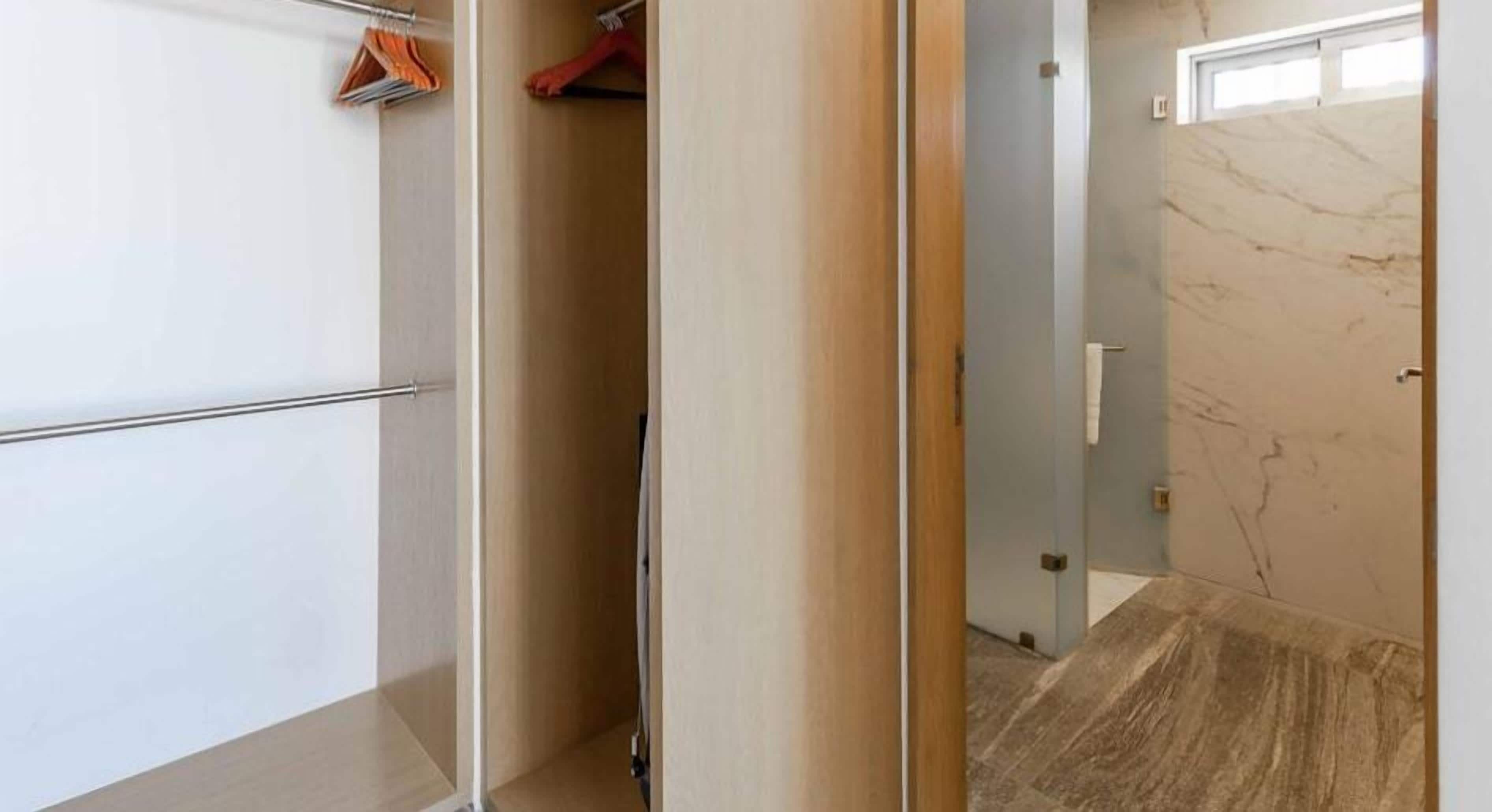 Een gang met een garderobe, een deur naar een badkamer met een marmeren vloer en een kapstok met kleding.