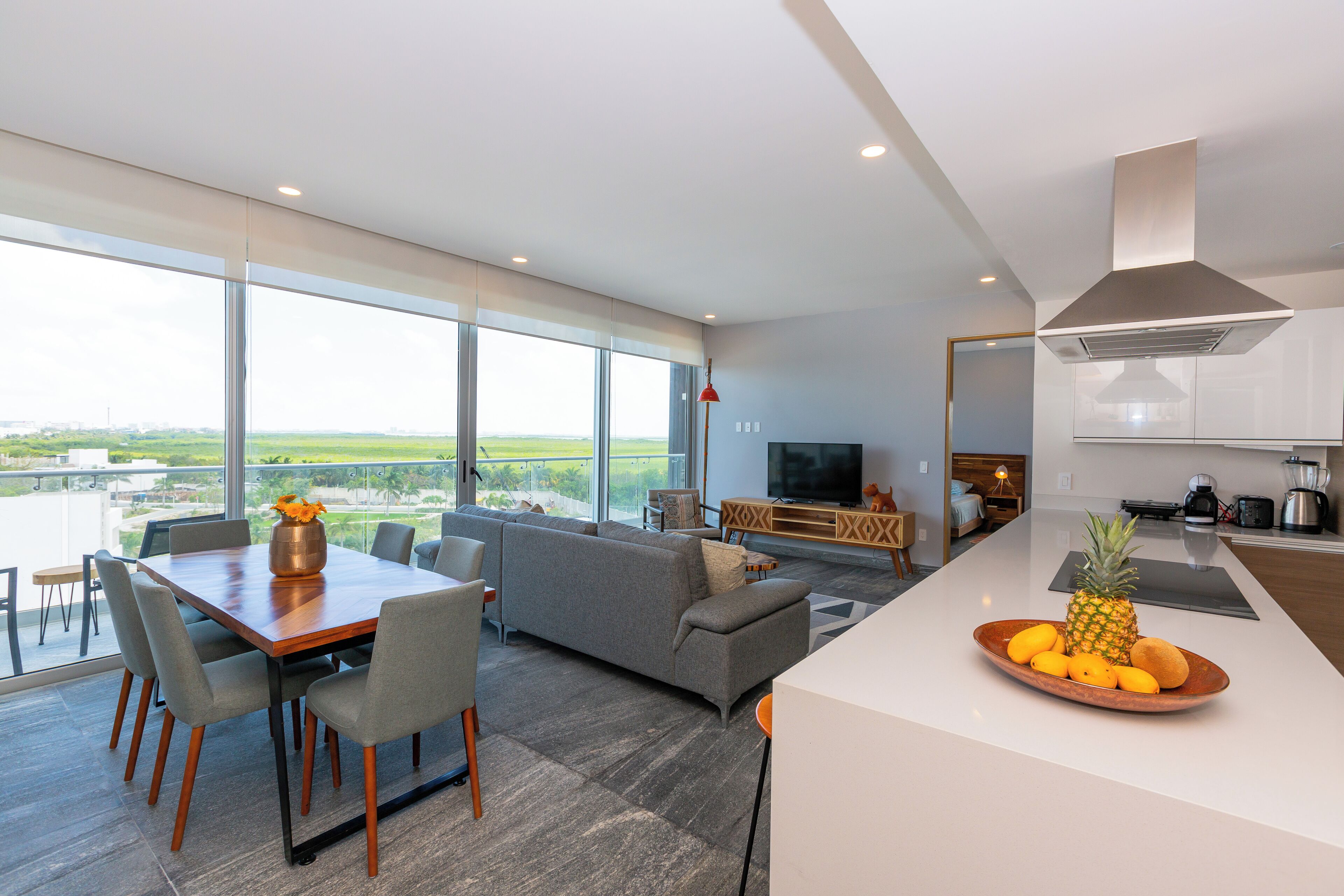 A modern living room with a large window, a dining area, and a kitchen.