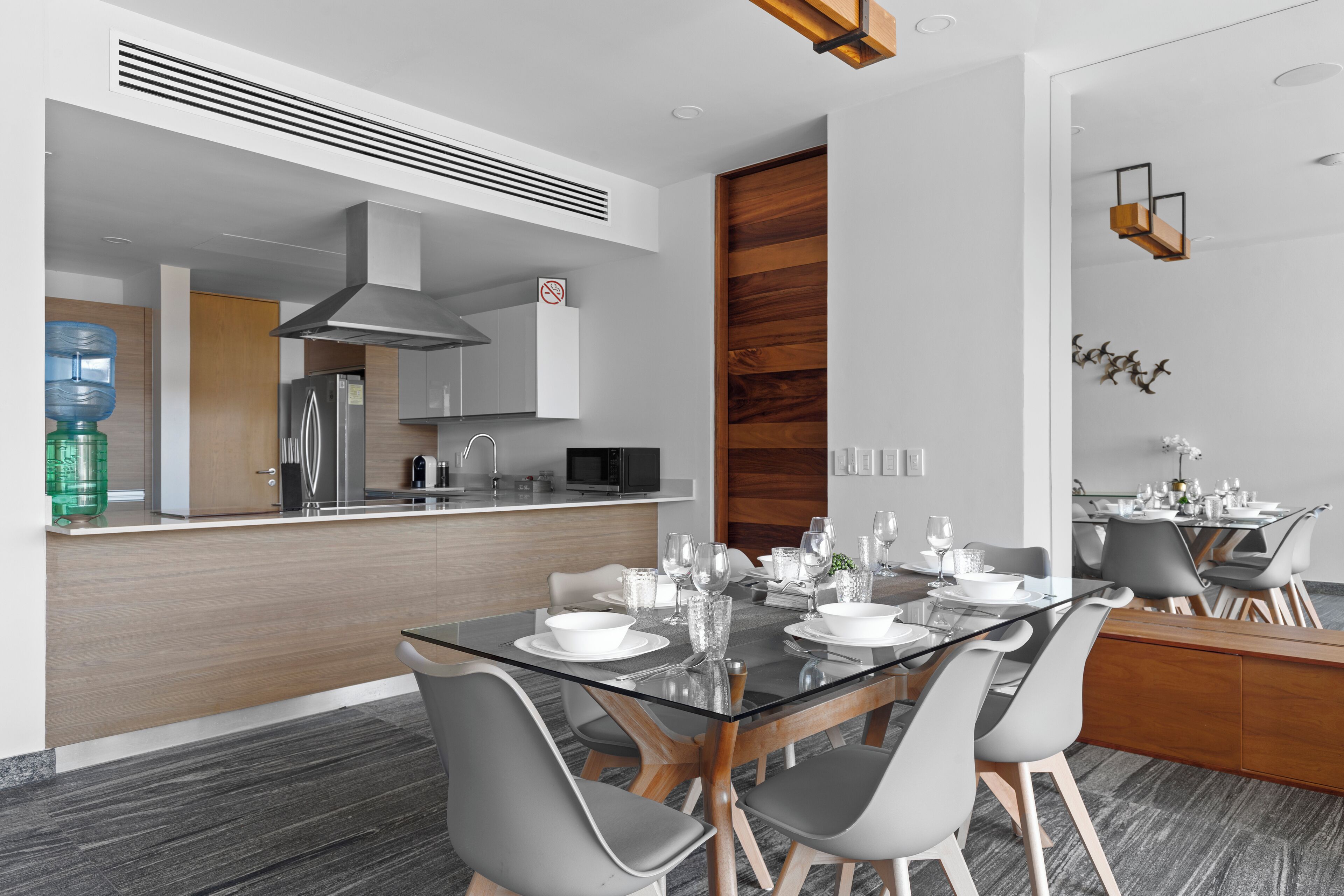 A modern kitchen with a central island, stainless steel appliances, and a dining area with a glass table and grey chairs.