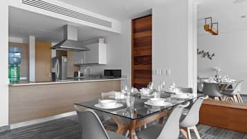 A modern kitchen with a central island, stainless steel appliances, and a dining area with a glass table and grey chairs.