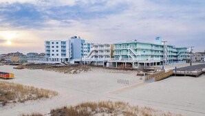 Een strandhotel met meerdere verdiepingen, een promenade en een strand op de voorgrond.