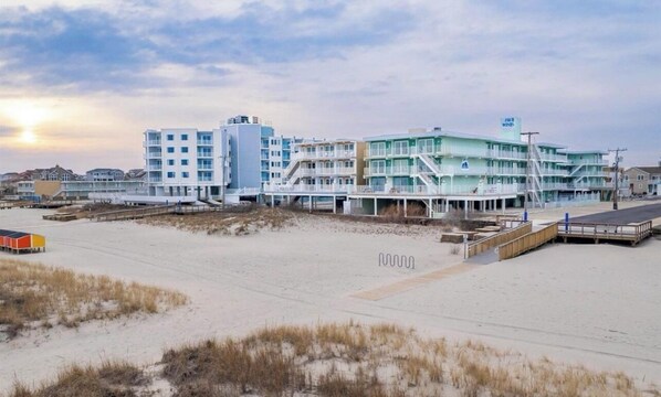 A beachfront hotel with multiple floors, a boardwalk, and a beach in the foreground.