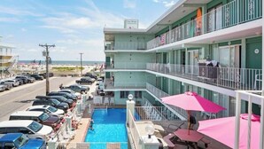 Een hotel met een zwembad op de begane grond, meerdere balkons en uitzicht op het strand.