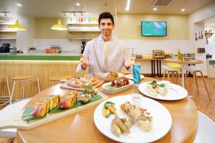 A restaurant with a chef presenting food, a variety of dishes on the table, and a TV in the background.
