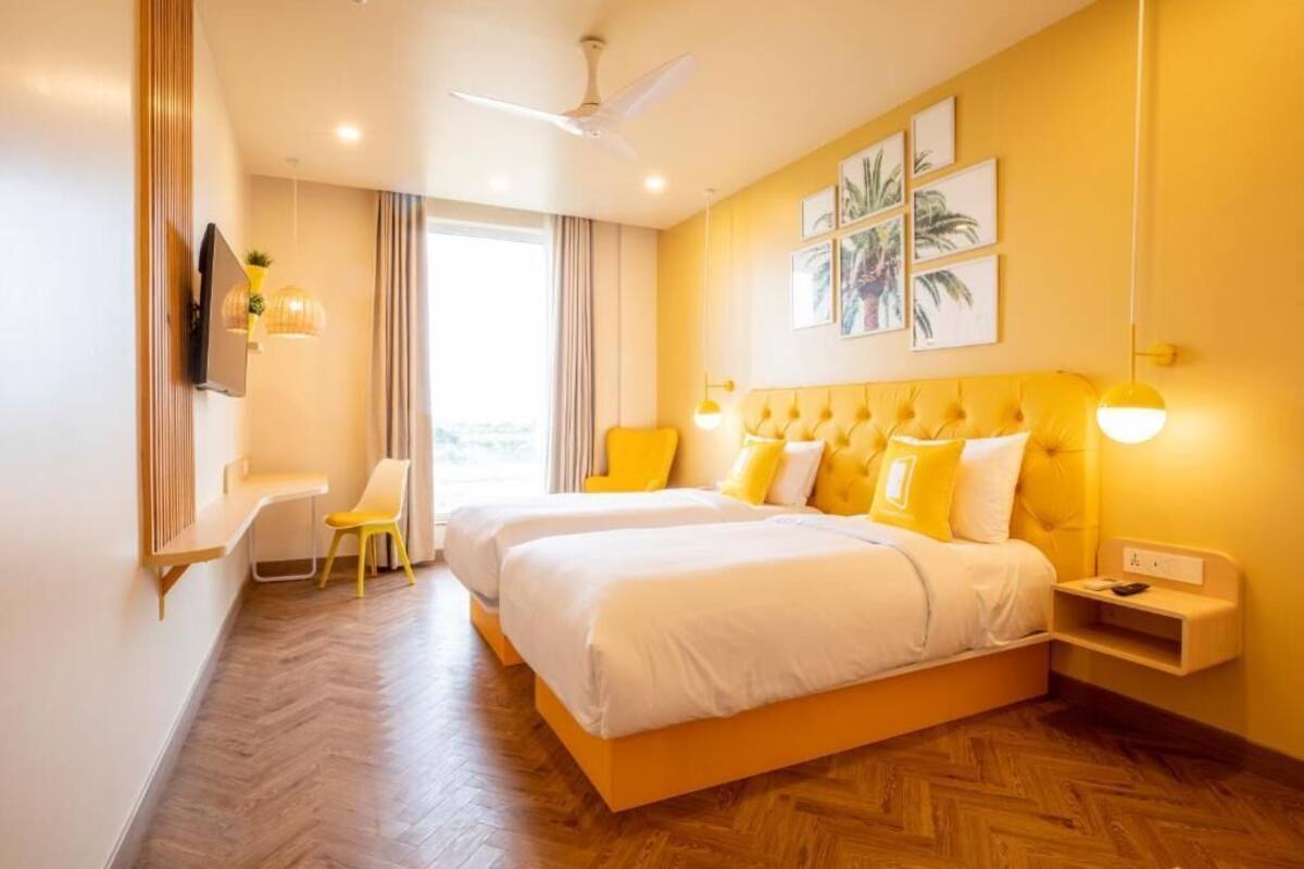 A hotel room with two beds, a desk, a chair, a TV, and a ceiling fan.
