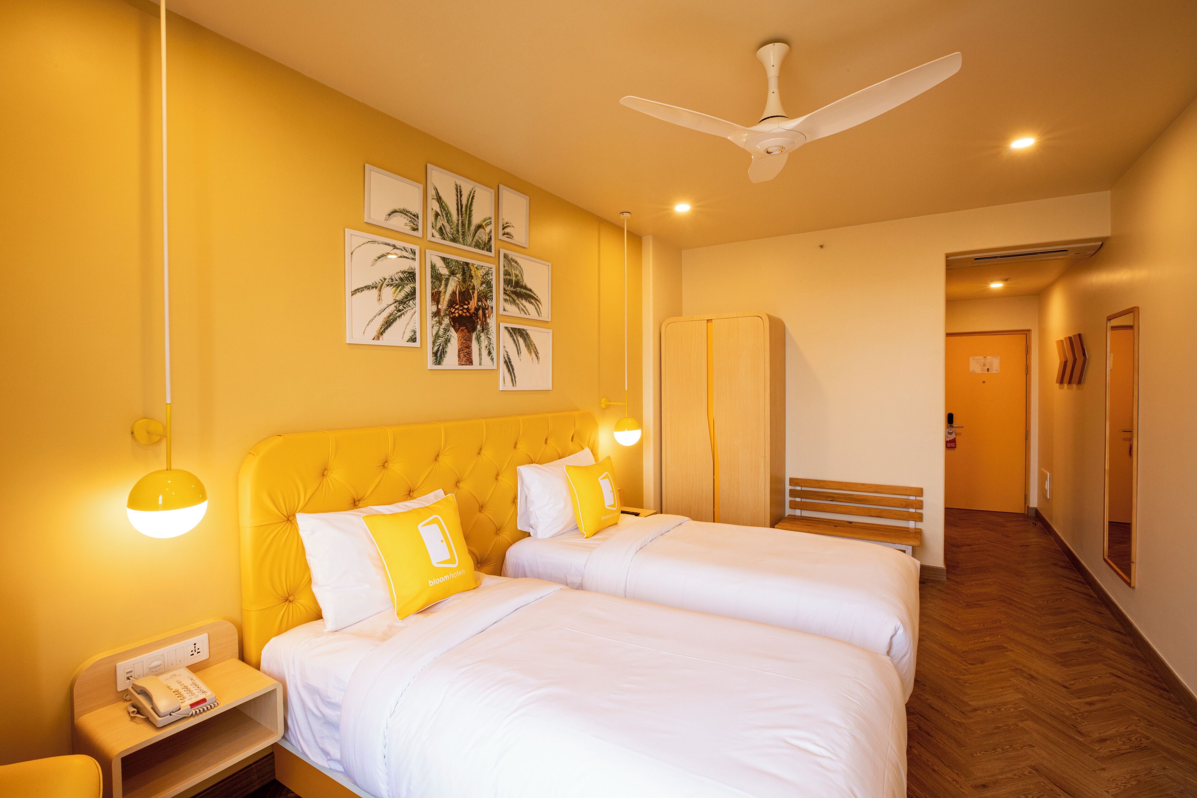 Una habitación de hotel con dos camas, ventilador de techo y obras de arte en la pared.
