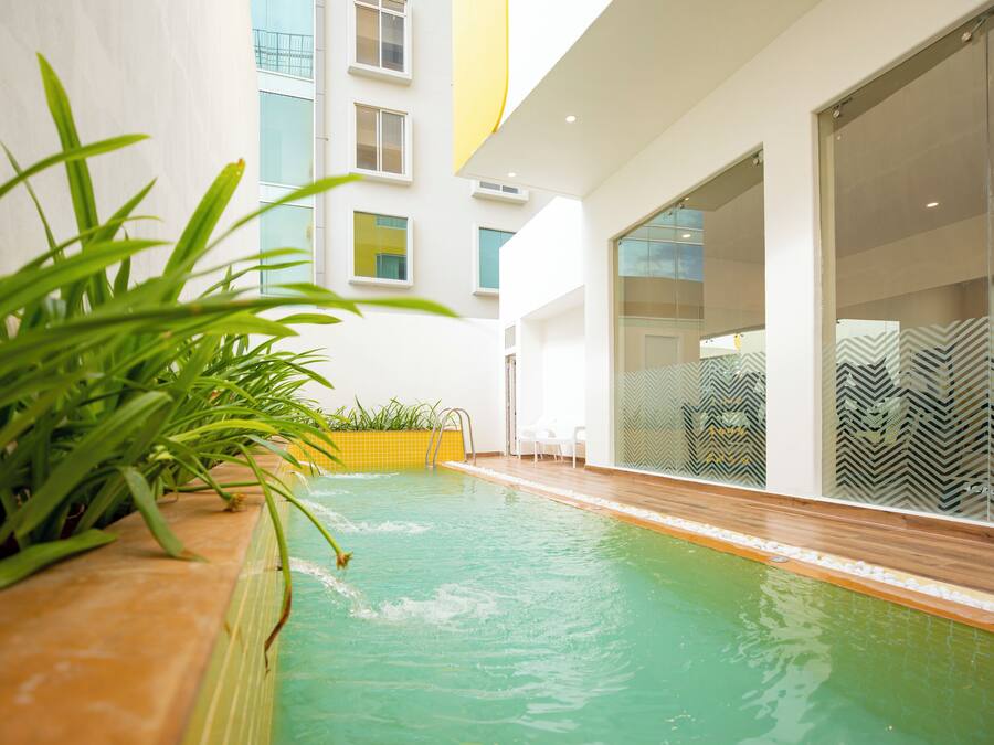 A modern indoor pool area with clear glass walls, a wooden deck, and potted plants.