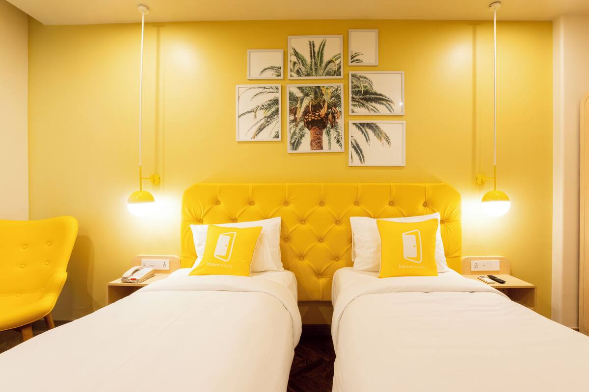 A hotel room with two beds, yellow walls, and a large window.