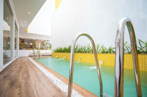 A modern indoor pool with clear water, a wooden deck, and a yellow-tiled wall.