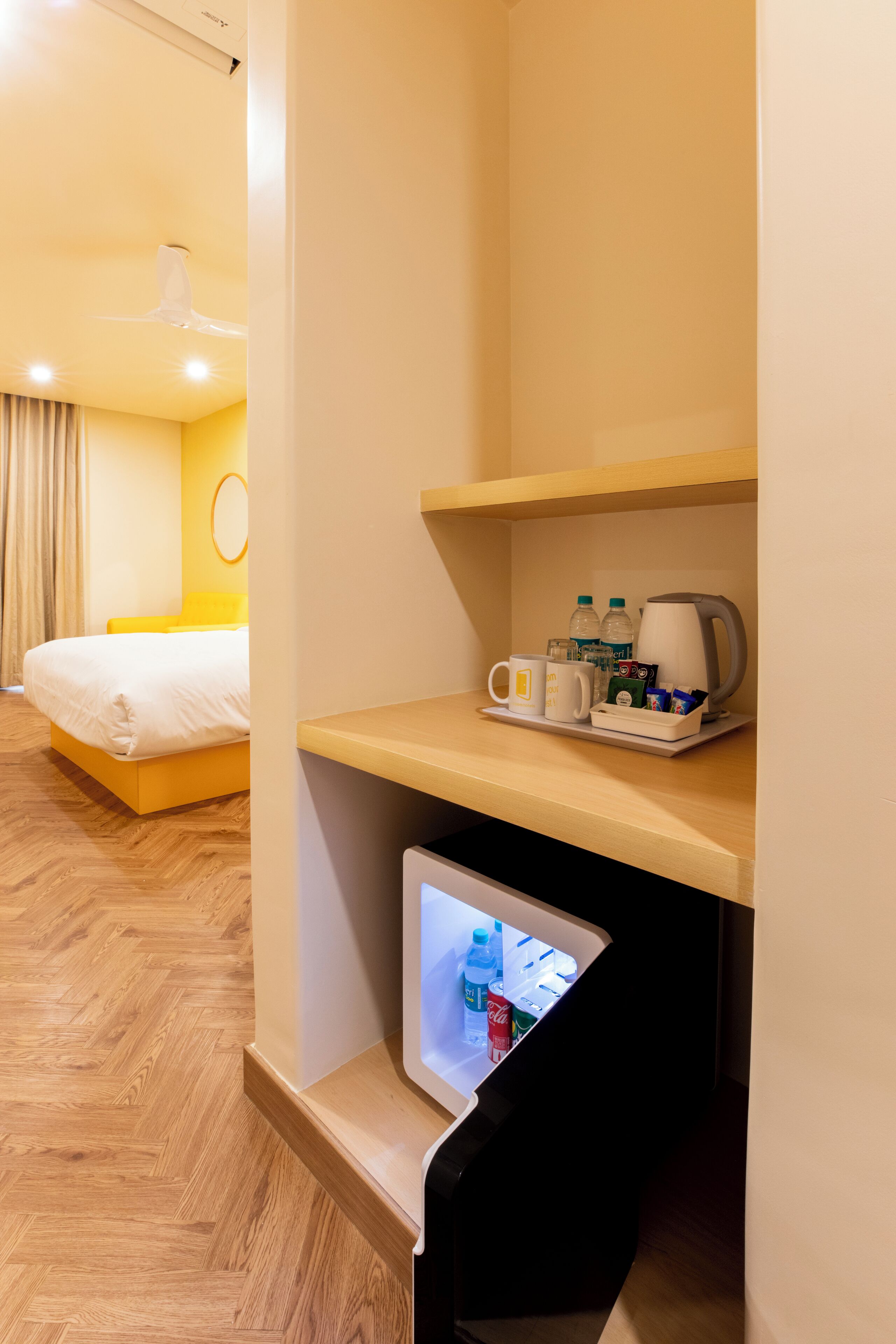 A hotel room with a bed, a desk with a coffee maker, and a mini-fridge.