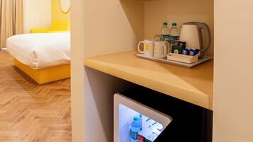 A hotel room with a bed, a desk with a coffee maker, and a mini-fridge.