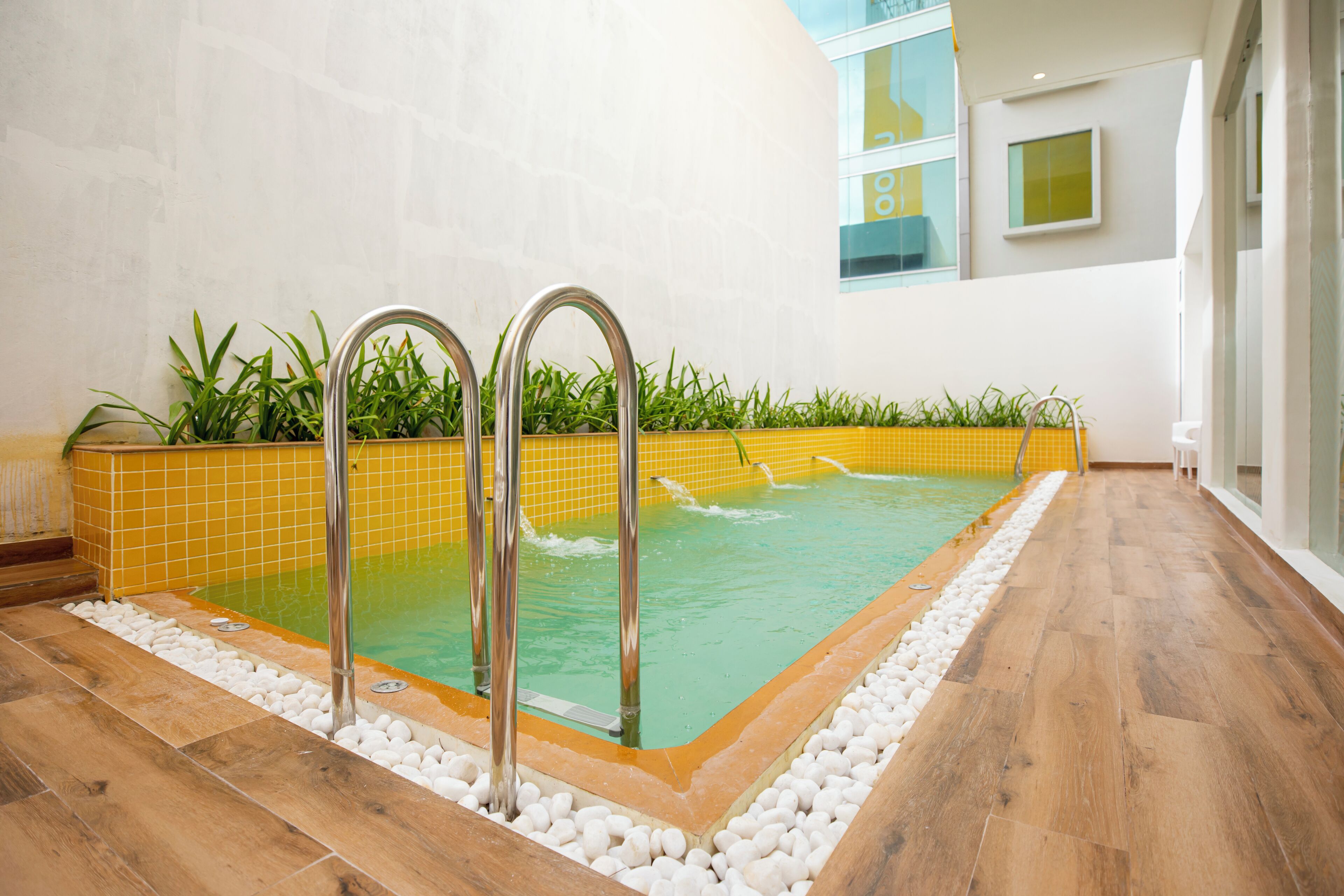 Una piscina interior con agua cristalina, rodeada por un borde de azulejos y una terraza de madera.