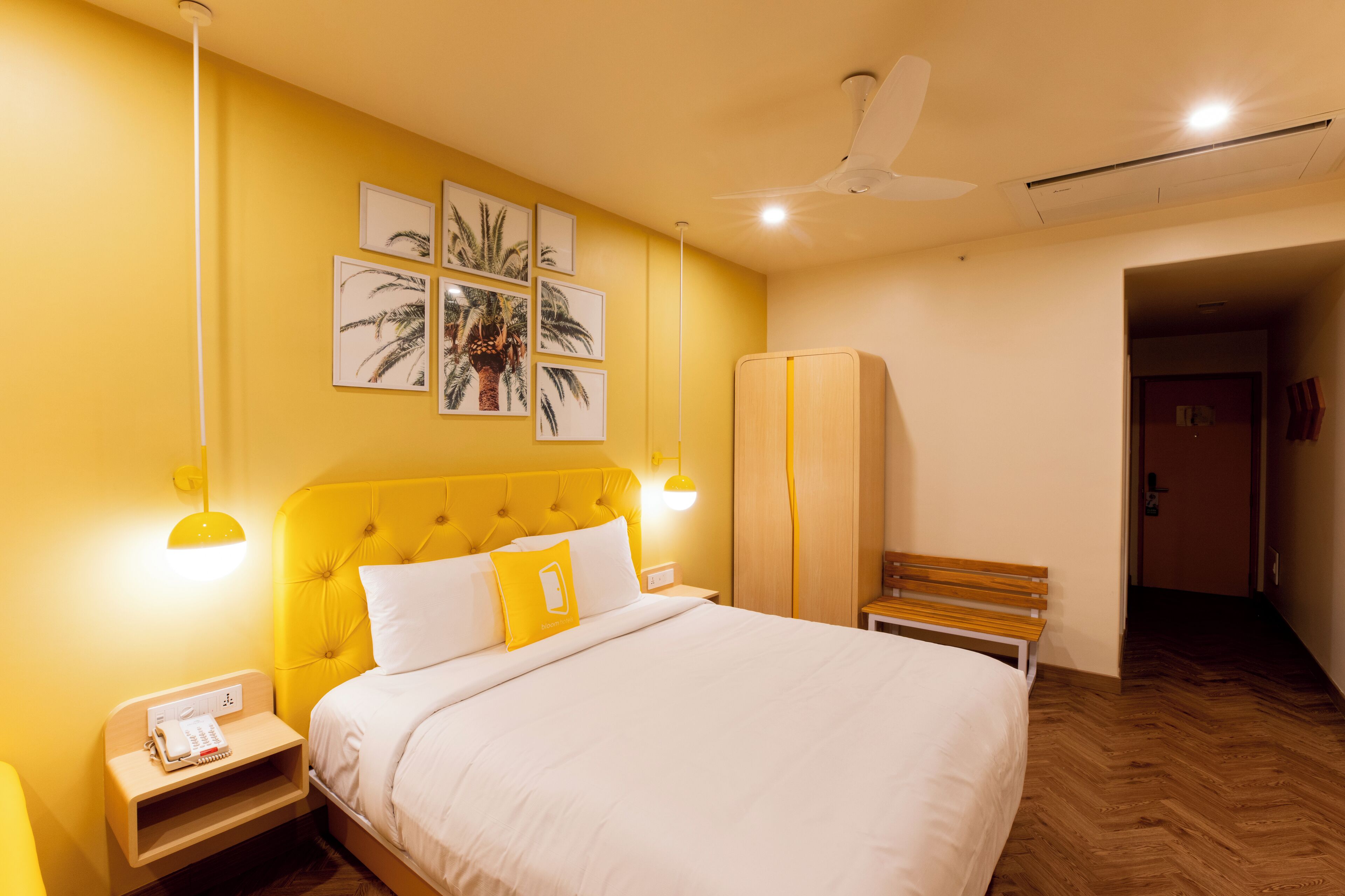 A hotel room with a yellow wall, a bed with white bedding, a wooden bench, and a wardrobe.