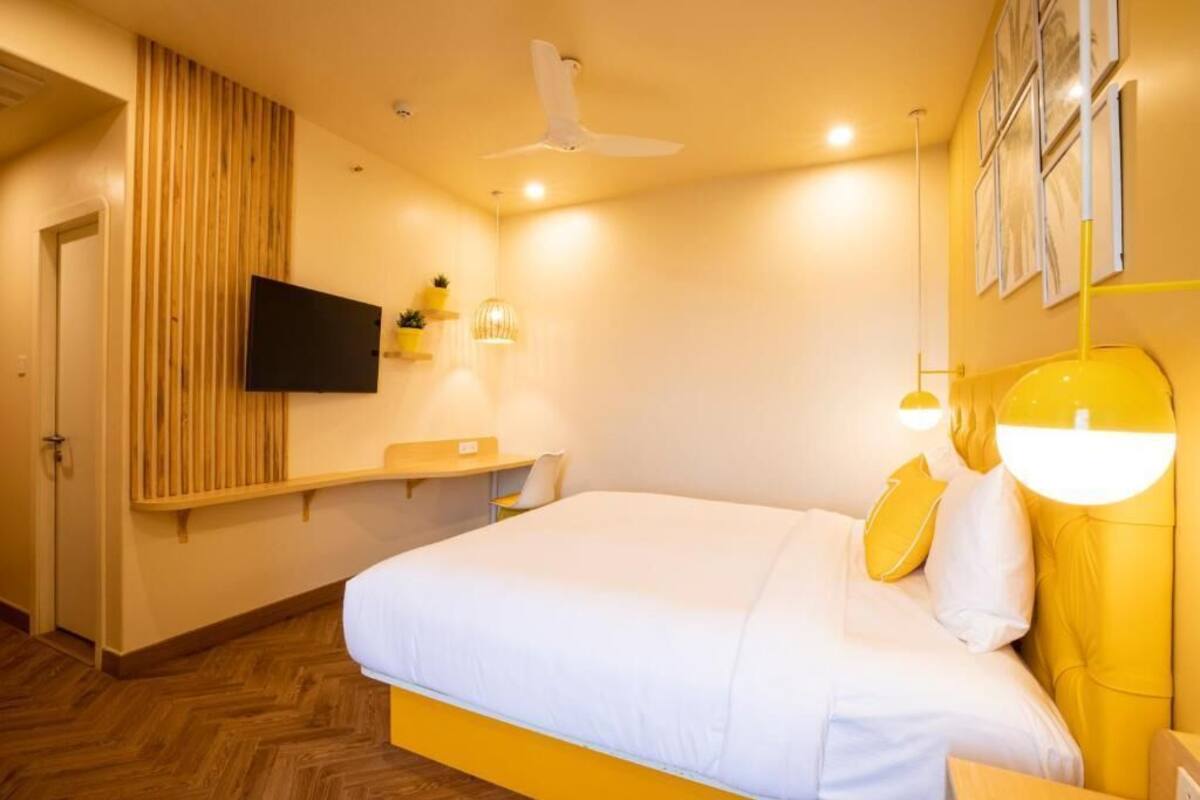 A hotel room with a bed, a mounted TV, a ceiling fan, and a wooden panel wall.