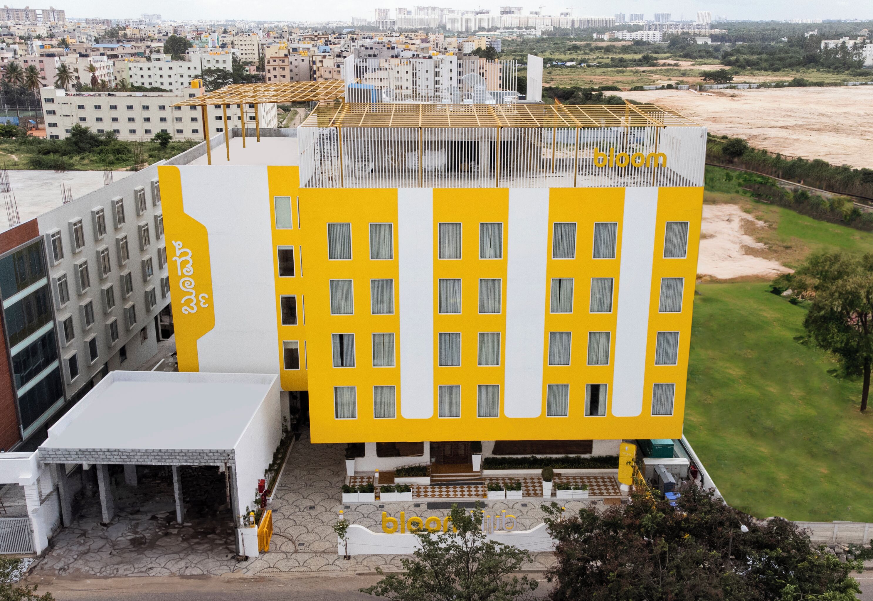 Un hotel moderno con fachada amarilla, varios pisos y una terraza en la azotea.